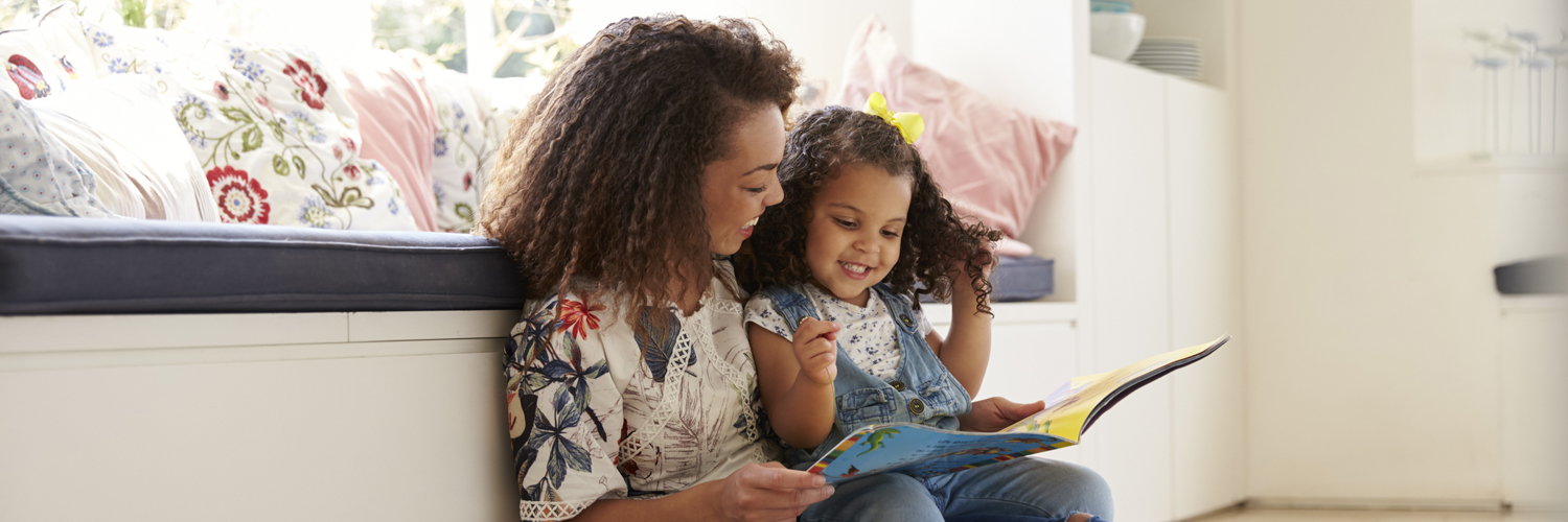 Mamma sitter på golvet med sin dotter och läser en bok