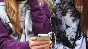 två kompisar håller i en smartphone. de är anonyma och man ser inte deras ansikten.