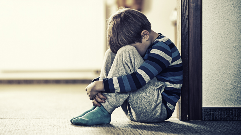 en pojke sitter ihopkrupen på ett golv i skolmiljö