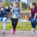 tre tjejer sitter på en parkbänk