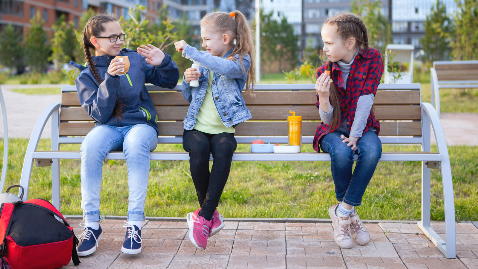 tre tjejer sitter på en parkbänk