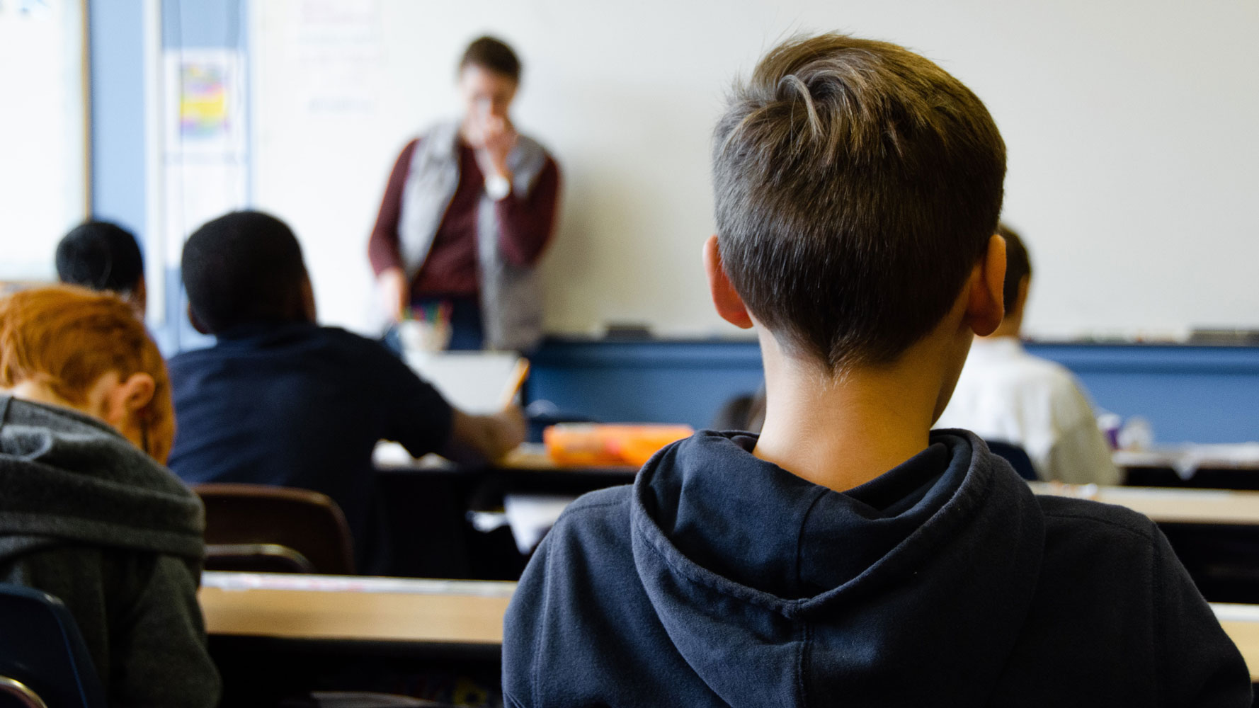 En pojke sitter med ryggen mot kameran i ett klassrum