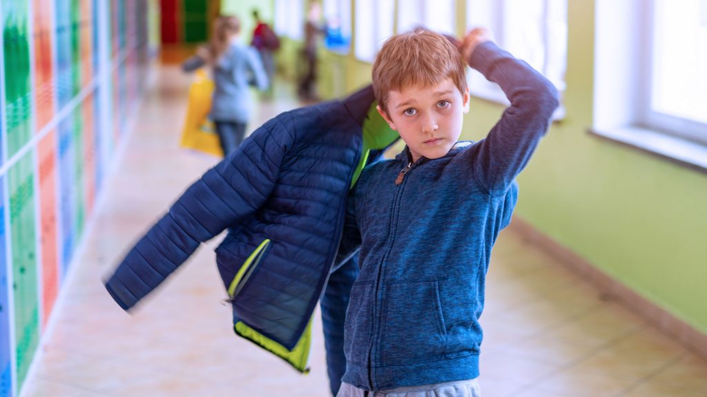 pojke som sätter på sig jackan i en skolkorridor.