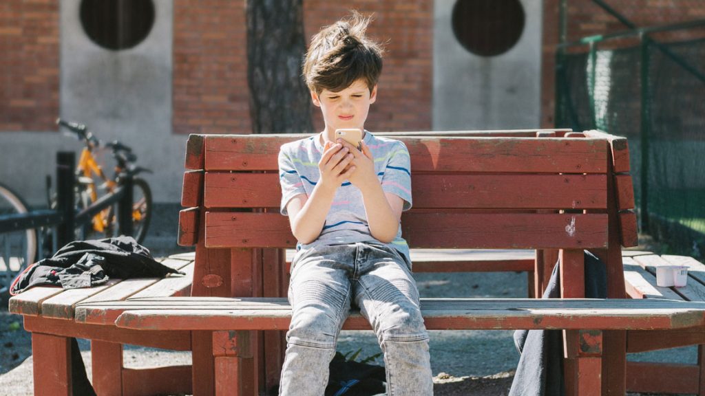 pojke sitter på en bänk med sin mobiltelefon