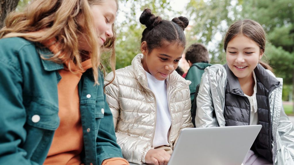 tre tjejer sitter utomhus med en dator