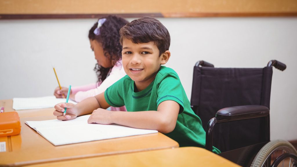 En pojke i rullstol ritar på ett block i ett klassrum